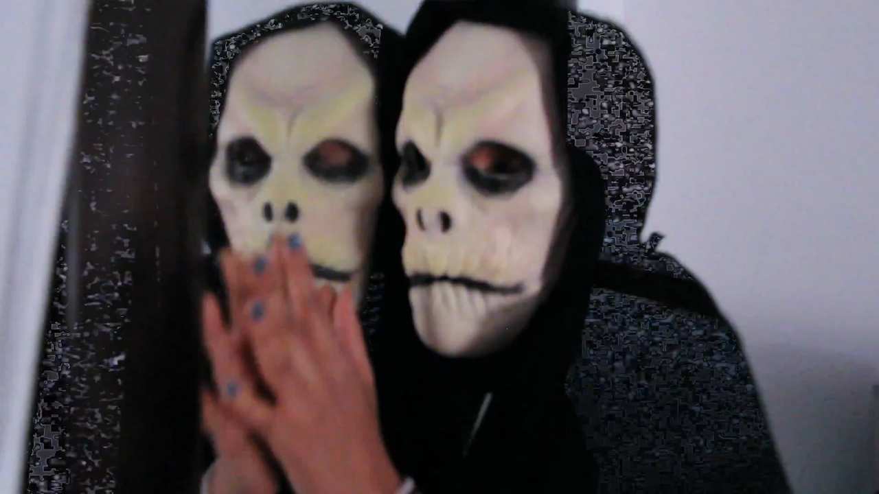 someone wearing a hood and skull mask by a mirror